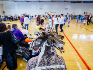 A person with a feathered headpiece looks out into a gymnasium filled with people.
