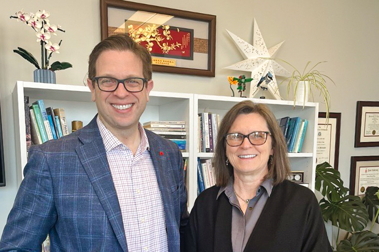 Two people stand in front of book shelves.