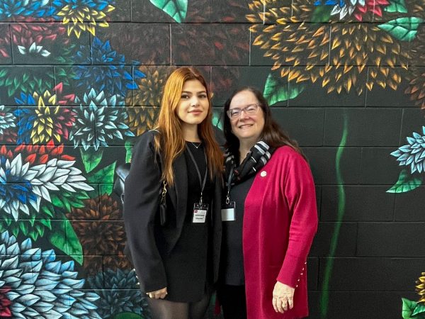 Two women standing in front of floral mural.
