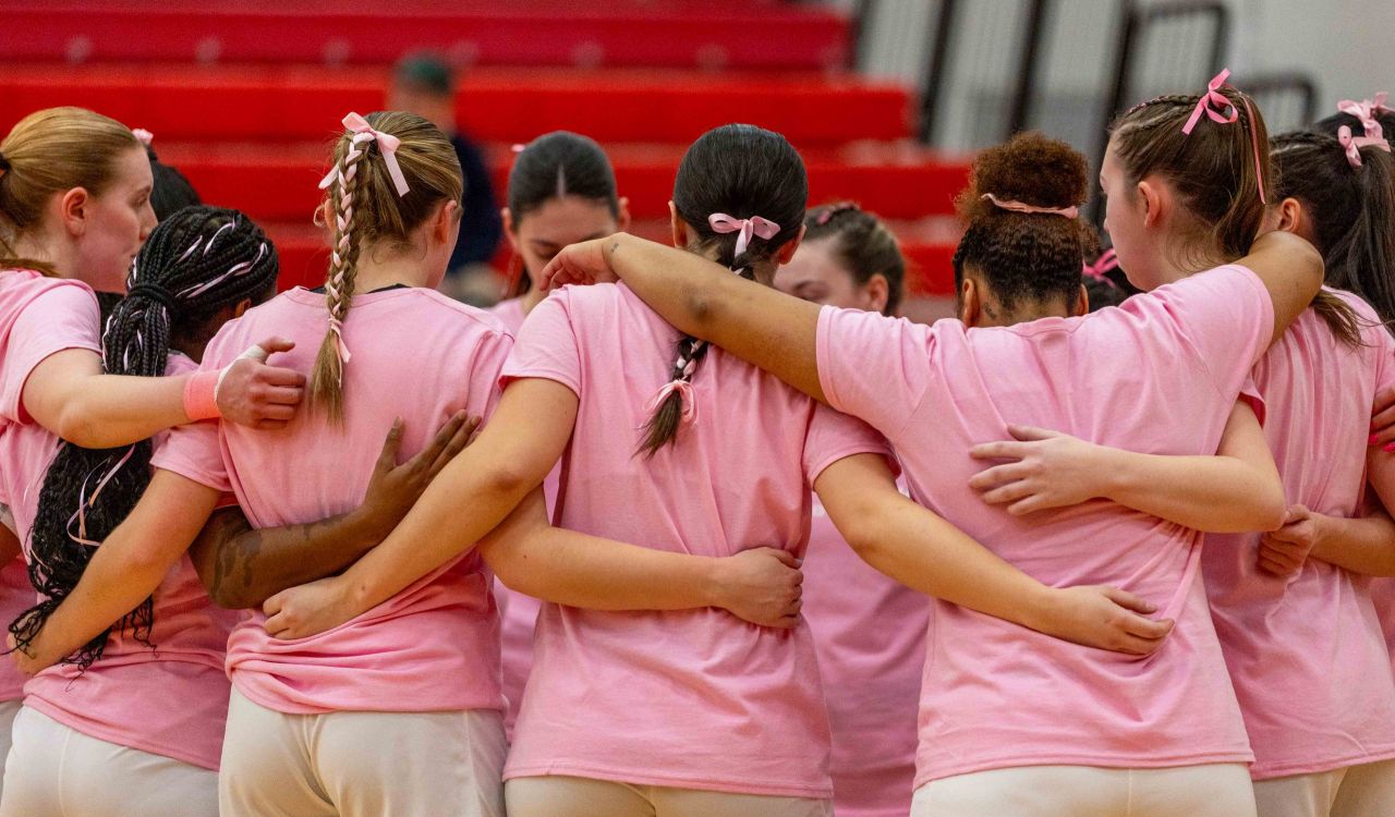 A group of Brock Badgers women’s basketball players wearing pink shirts huddle before the 2025 Shoot for the Cure Game.