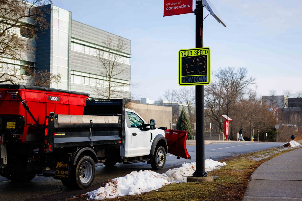 A truck with a plough drives down a campus road.