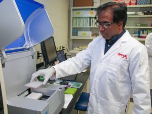 A man in a white lab coat picks up small a tray of vials from a scientific machine while conducting grapevine virus testing.