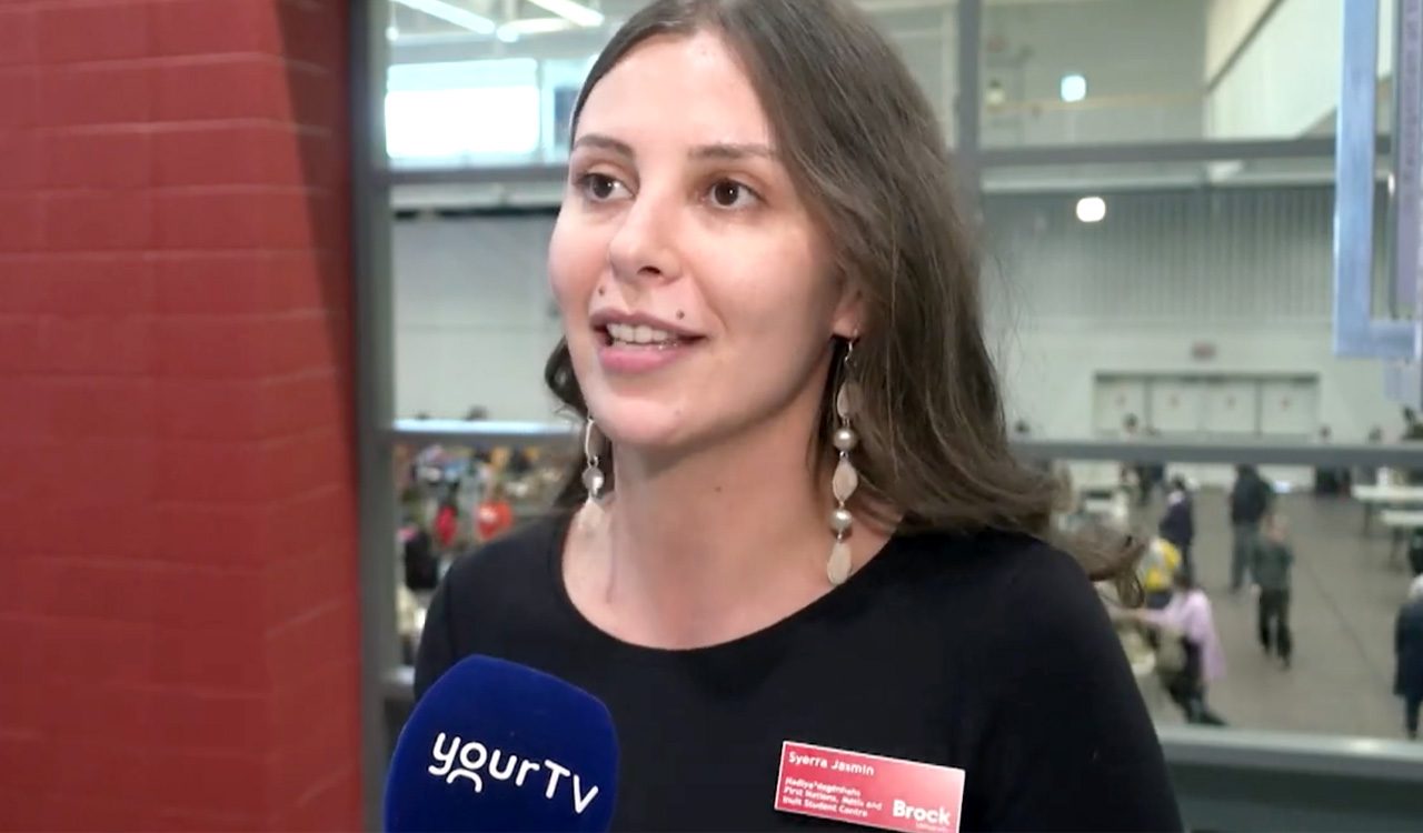 Woman in a black shirt in front of gymnasium does a television interview.