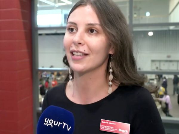 Woman in a black shirt in front of gymnasium does a television interview.