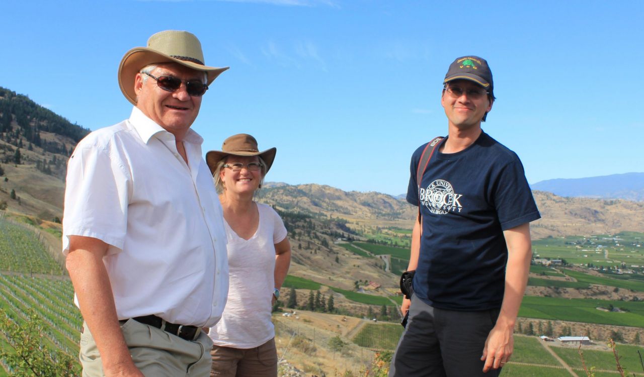 Three people stand side by side in a field in British Columbia’s wine region.