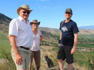 Three people stand side by side in a field in British Columbia’s wine region.