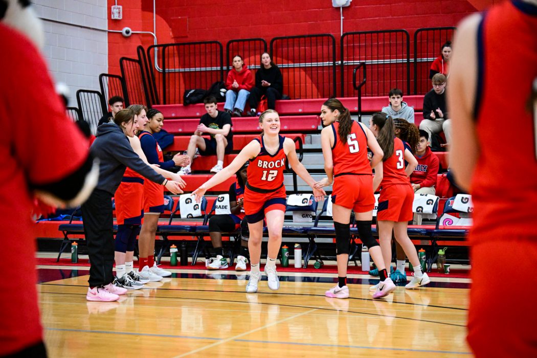 A young woman in a basketball uniform runs onto a basketball court with team members around her.