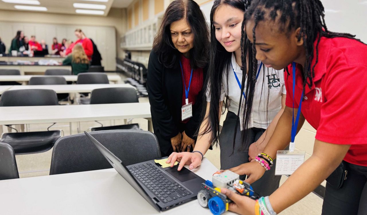 Two students and a professor look at a computer together.