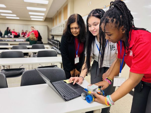 Two students and a professor look at a computer together.