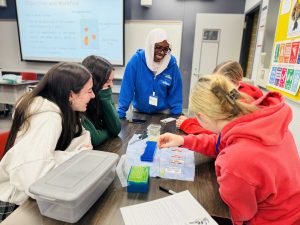 Students in a science lab sit at a table listening to a workshop leader.