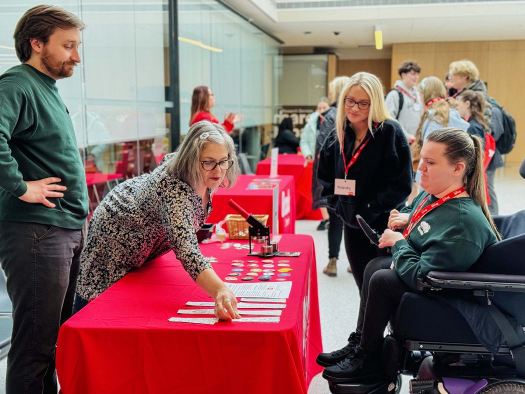A young person using a wheelchair and three other people have a conversation during an information fair at a university.