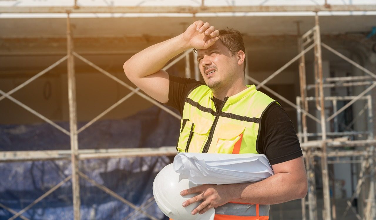 A man in safety equipment works outside in the heat.