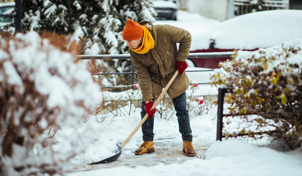 Man in yellow hat and winter coat shovels snow.