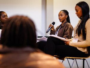 Two women sit on chairs while speaking to an audience.