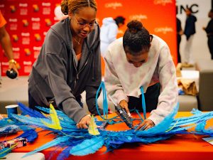 Two people create carnivale headdresses.