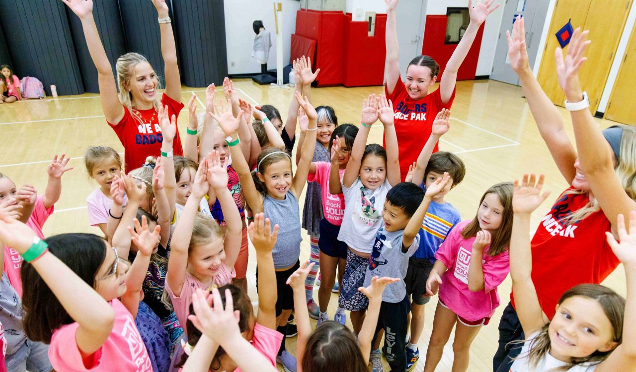 A large group of young girls cheer at a summer camp.