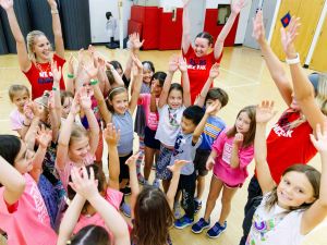 A large group of young girls cheer at a summer camp.