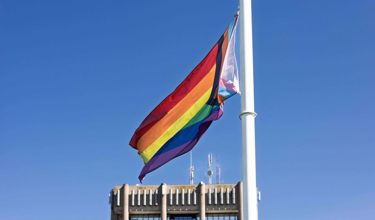 A Pride flag flies with a blue sky in the background.