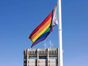A Pride flag flies with a blue sky in the background.
