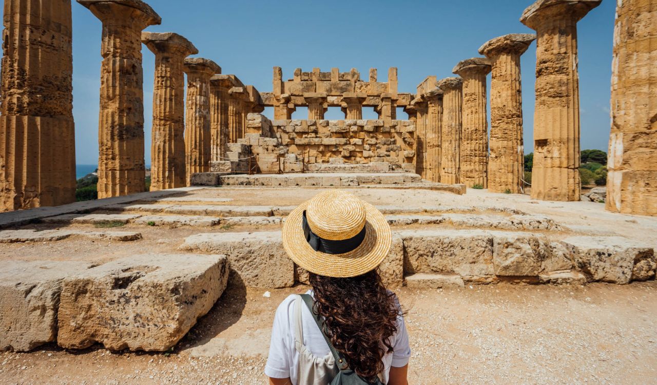 A woman, seen from behind, looks at ancient ruins.