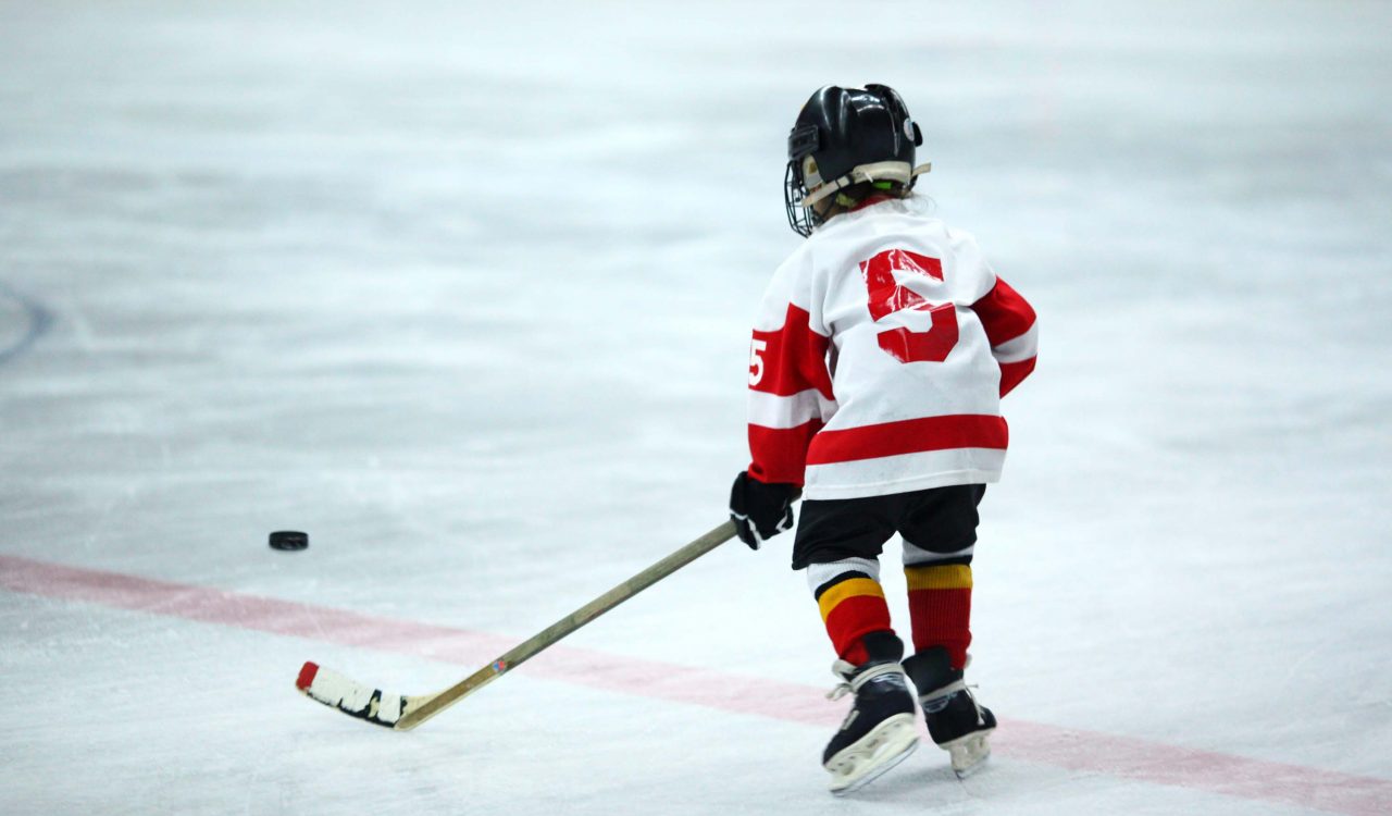 A small child wearing hockey equipment and jersey 5 on the ice.