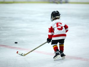 A small child wearing hockey equipment and jersey 5 on the ice.