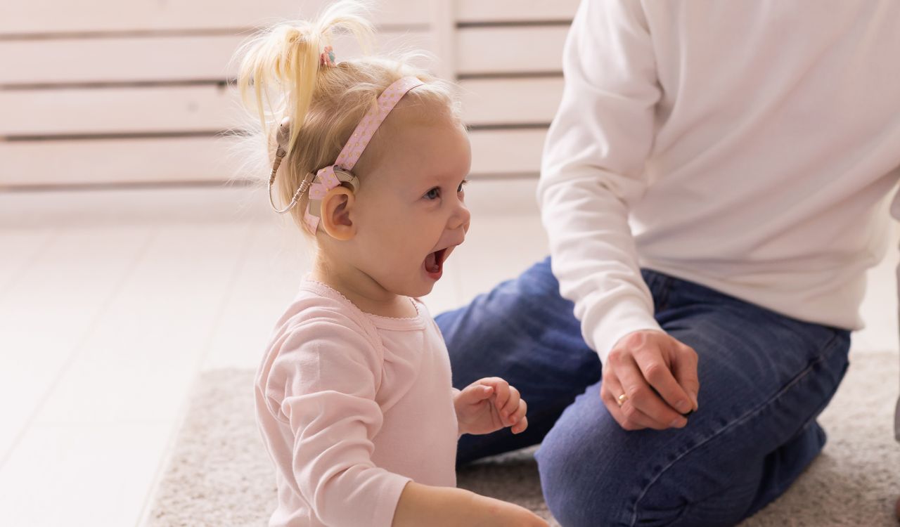 A baby with cochlear implants plays in the living room of their home.