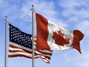 The American and Canadian flags fly against a blue sky.