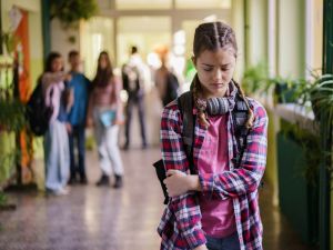 A teenager walks down the hall looking sad while other teenagers point and laugh behind them.