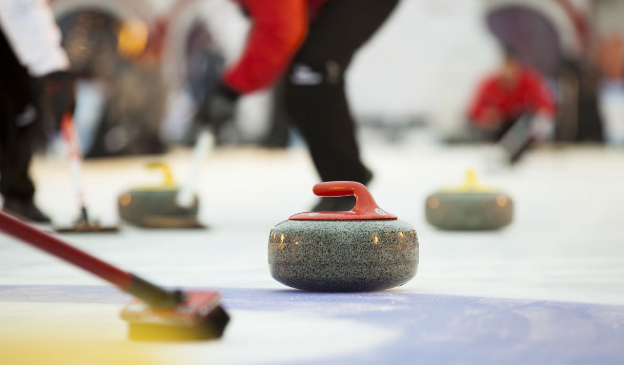 Close-up of curling stone on ice with players in the background.