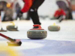 Close-up of curling stone on ice with players in the background.