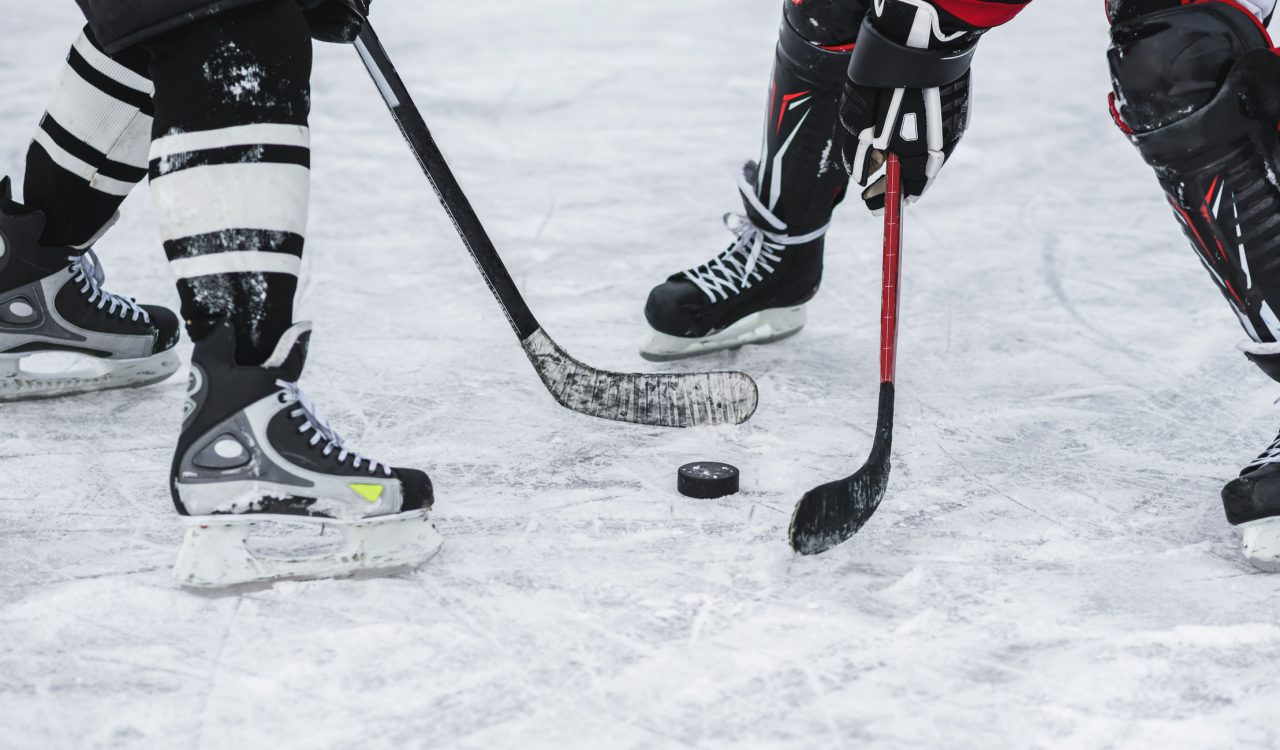 Close-up of a puck and the feet of two hockey players on an ice rink.