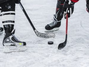 Close-up of a puck and the feet of two hockey players on an ice rink.