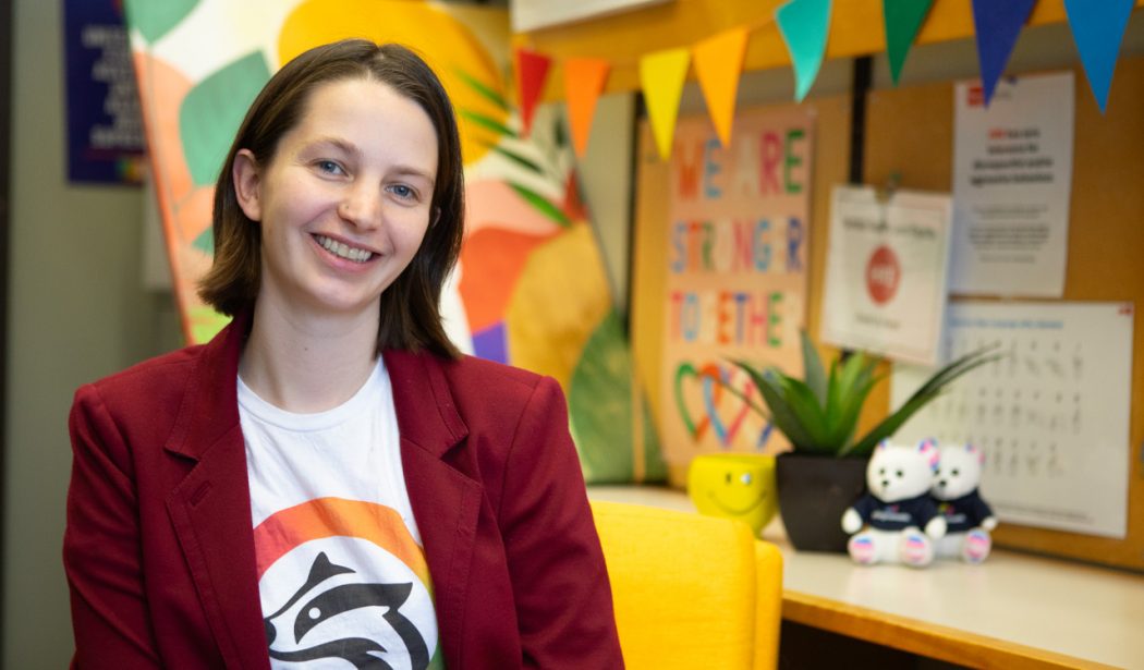 A woman sits at a desk with colourful decorations behind her.