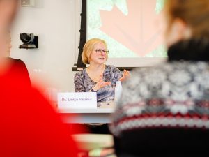 Liette Vasseur speaks while seated at a panel table, gesturing with her hands during a discussion.