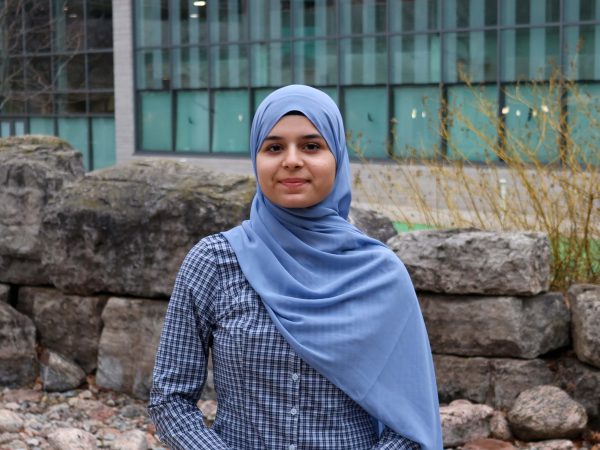 A young woman wearing a hijab poses for a photo outside a building.