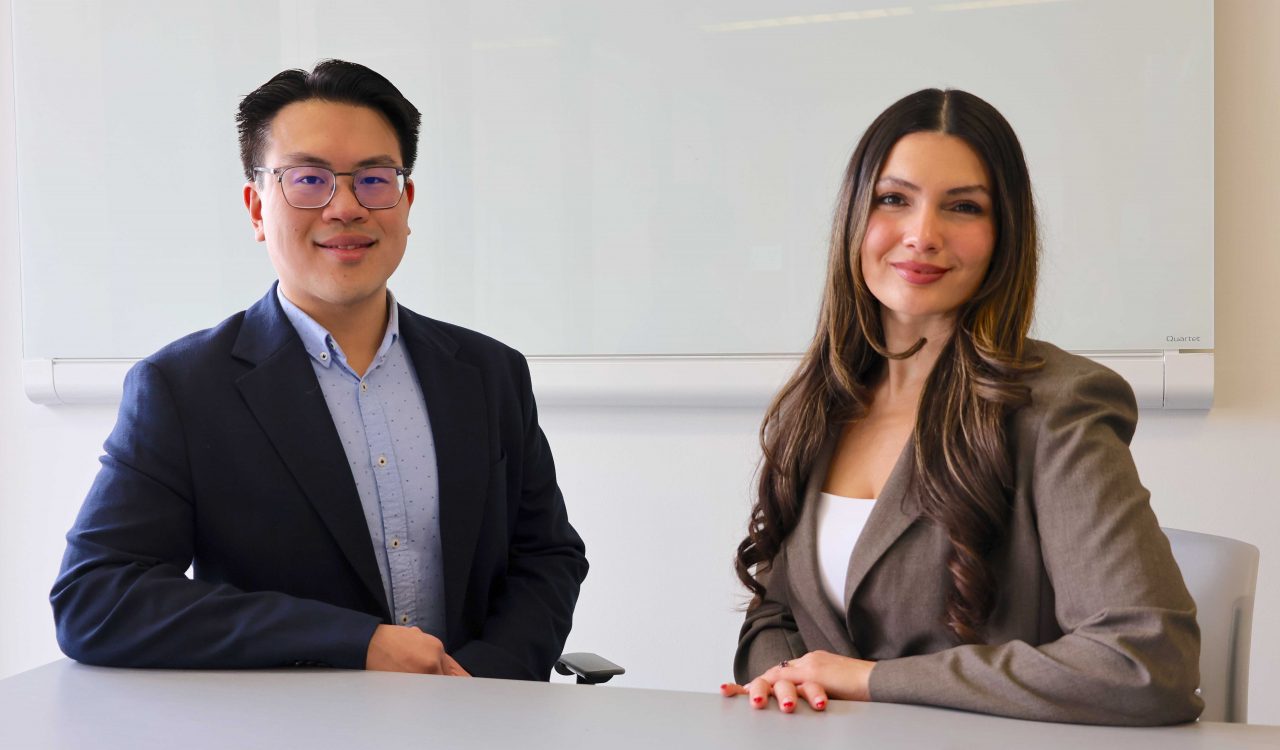 Two people sit at a table in a university classroom.