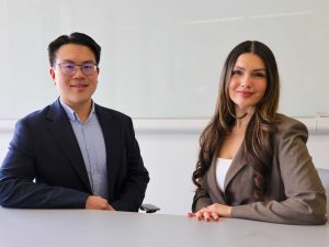 Two people sit at a table in a university classroom.