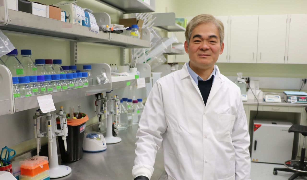 A man in a lab coat stands in a lab.