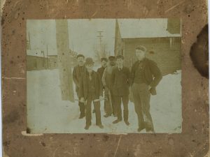 An aged photograph shows men standing together outdoors.