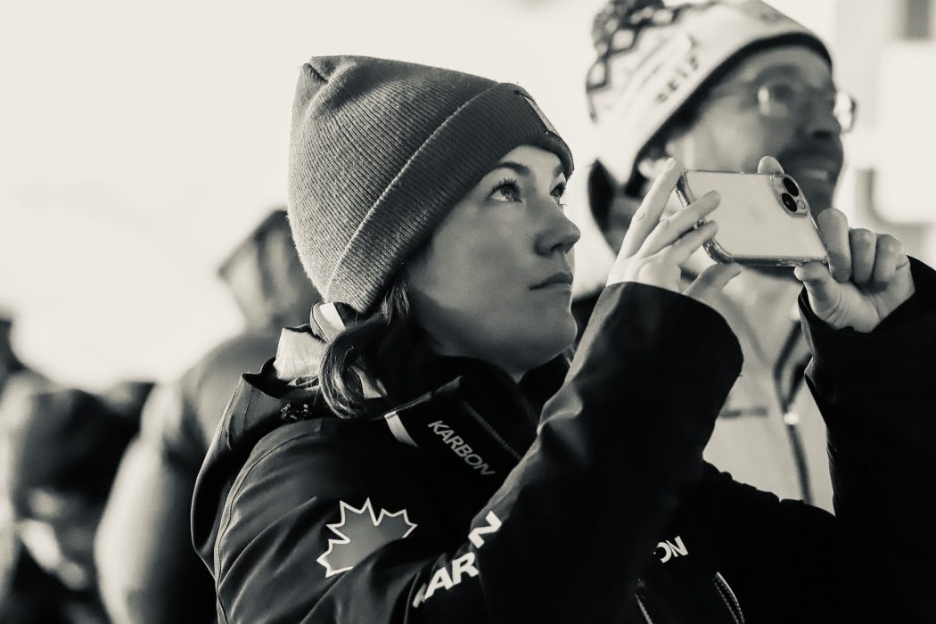 A woman in winter clothing takes pictures with a phone.