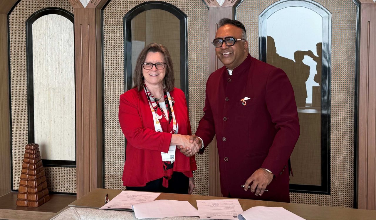 Two people shake hands beside a table covered in documents after signing a contract.