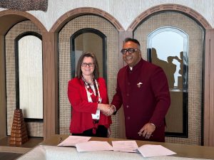 Two people shake hands beside a table covered in documents after signing a contract.