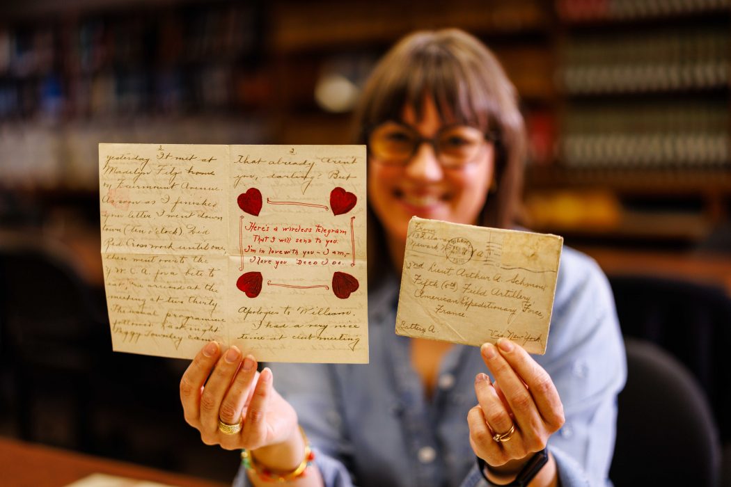 A woman holds up at archival materials including letters and drawings.
