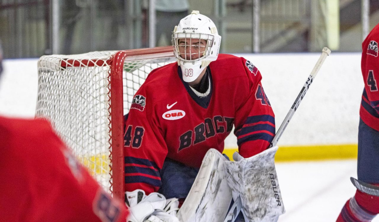 A goalie stands in front of a net during an ice hockey game.