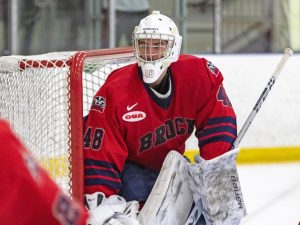 A goalie stands in front of a net during an ice hockey game.