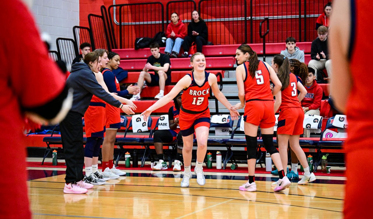 A woman in a basketball uniform extends her hands to high-five supporters in a gym.