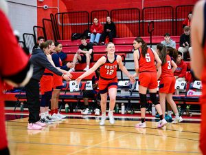 A woman in a basketball uniform extends her hands to high-five supporters in a gym.