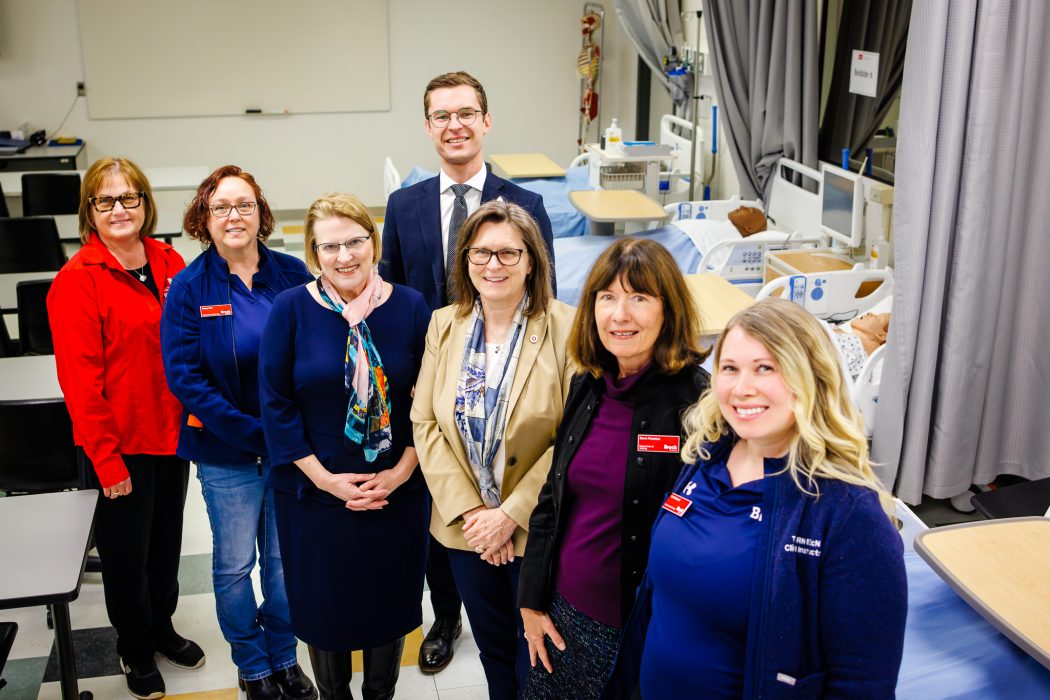A group of people stand in a nursing lab.