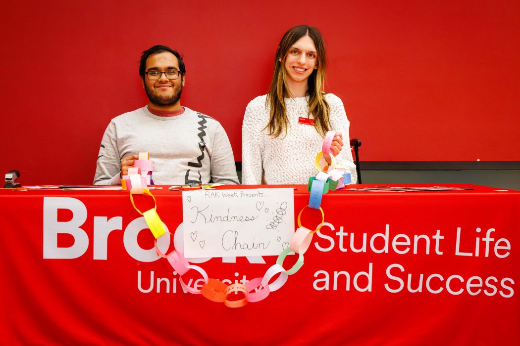 Two people sit at a table in front of a red wall.